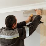Man is cutting wallpaper. Maintenance repair works renovation in the flat. Apartment renovation and restoration idea indoors.